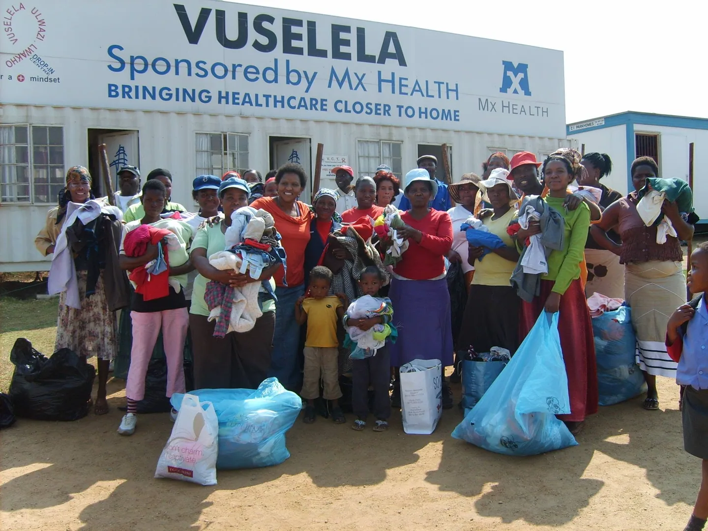 A group of people holding clothing outside a building with Vuselela signage.