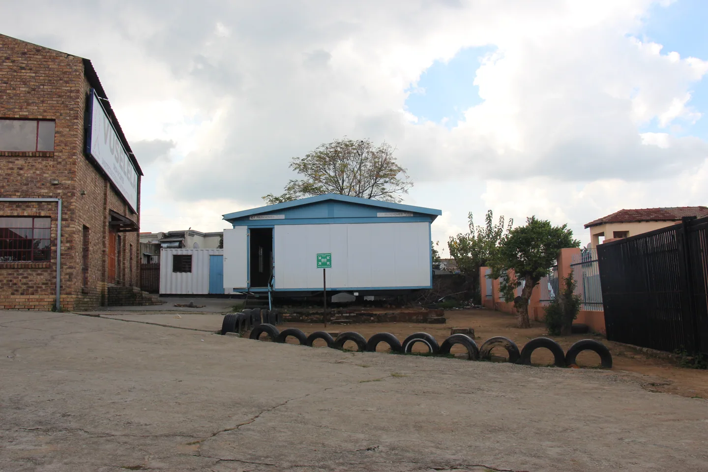 White portable building with blue trim and an open door beside the courtyard.