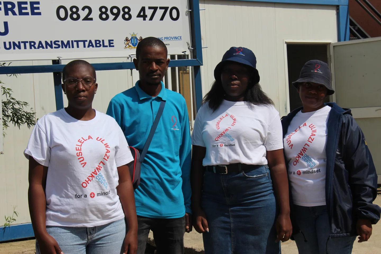 Four people in Vuselela clothing standing outside a white-and-blue building.